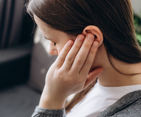 Junge Frau hält sich ihr Ohr zu.