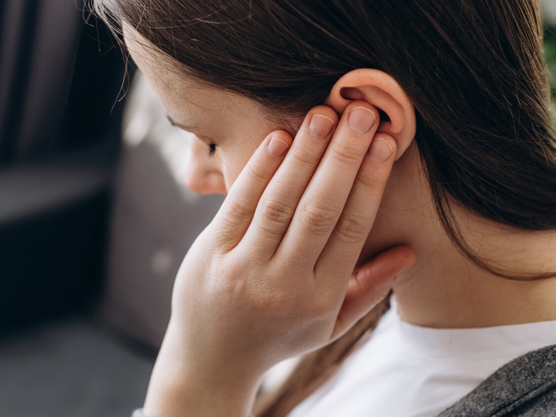 Junge Frau hält sich ihr Ohr zu.