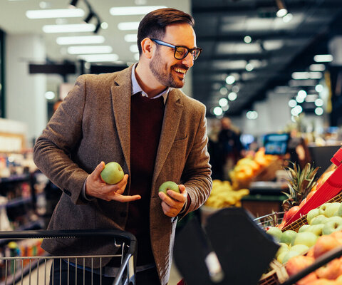 Ein Mann steht in einem Supermarkt in der Gemüseabteilung und kauft ein.