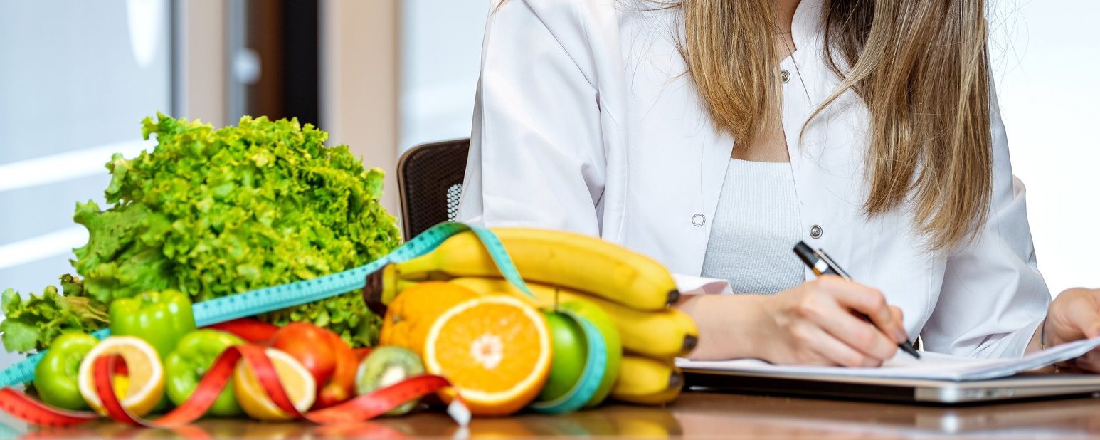 Eine Frau sitzt am Tisch und macht sich Notizen. Daneben liegt ein Haufen Gemüse und ein Maßband.