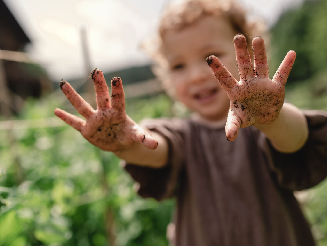 Ein Kind steht im Garten und hält seine erdigen Hände in die Höhe.