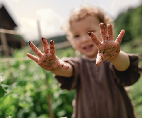 Ein Kind steht im Garten und hält seine erdigen Hände in die Höhe.