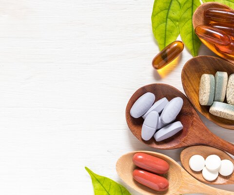 Auf einem weißen Untergrund liegen fünf Holzlöffel mit verschiedenen Arten von Tabletten und Kapseln. 