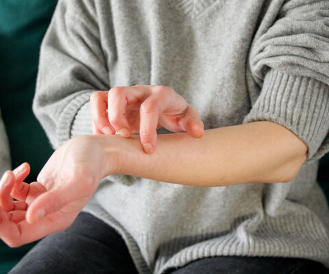 Eine Frau kratzt sich am Unterarm.