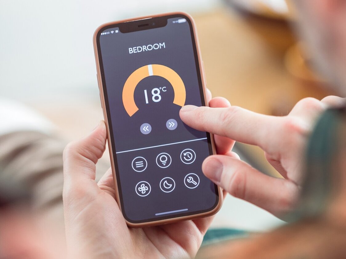 Ein Mann hat ein Handy mit einer Heizungs-App in der Hand.
