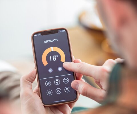 Ein Mann hat ein Handy mit einer Heizungs-App in der Hand.