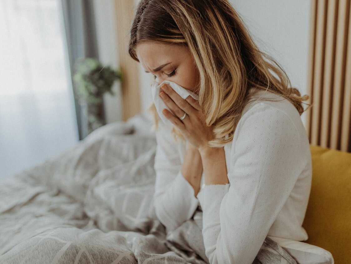 Frau schnaubt sich im Bett die Nase