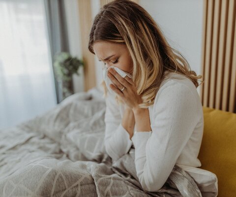 Frau schnaubt sich im Bett die Nase
