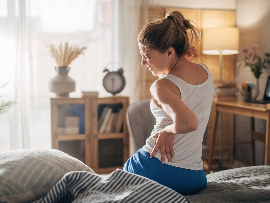 Frau sitzt im Bett mit Schmerzen im unteren Rücken