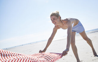 Eine Frau breitet am Strand ein Handtuch aus.