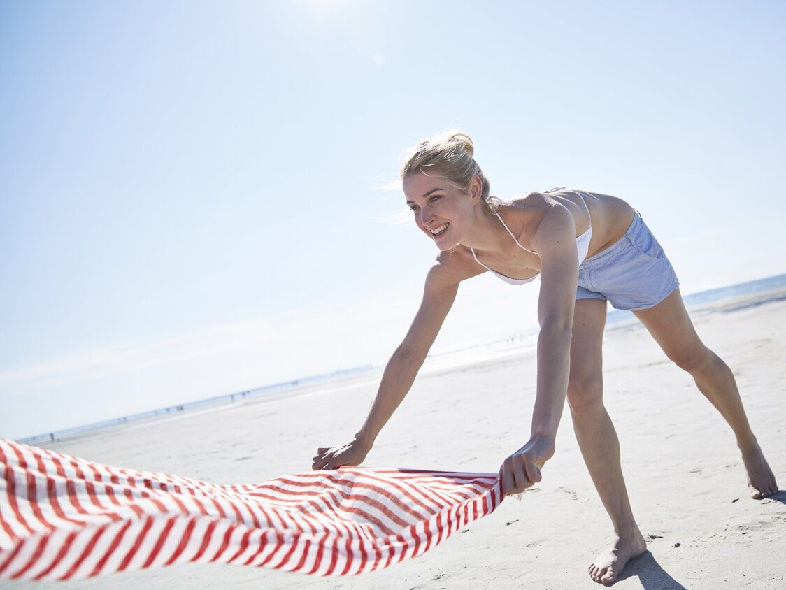 Eine Frau breitet am Strand ein Handtuch aus.