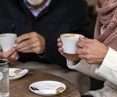 Ein Paar sitzt an einem Tisch und trinkt einen Kaffee. Auf der Untertasse liegt je ein Keks.