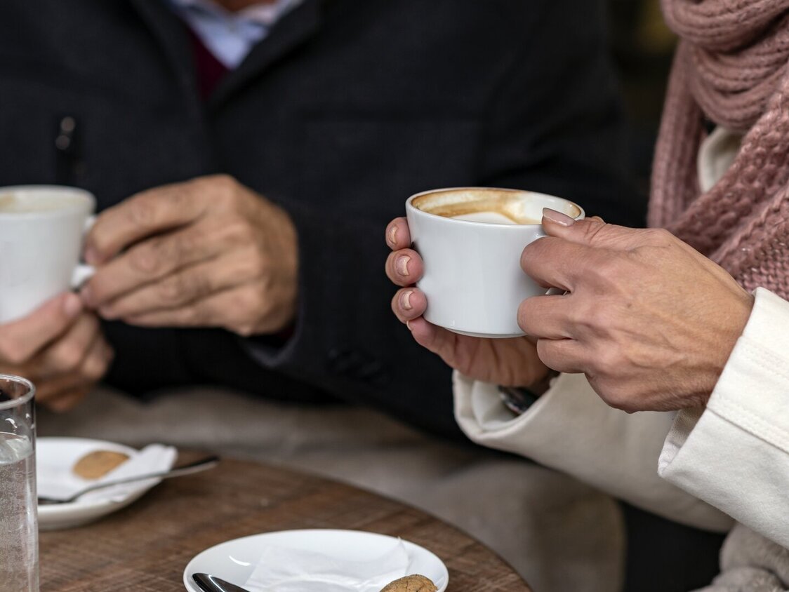 Ein Paar sitzt an einem Tisch und trinkt einen Kaffee. Auf der Untertasse liegt je ein Keks.