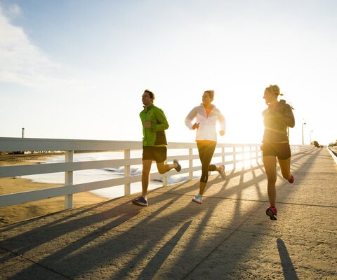 Drei Personen laufen bei Sonnenschein an der Strandpromenade entlang. 