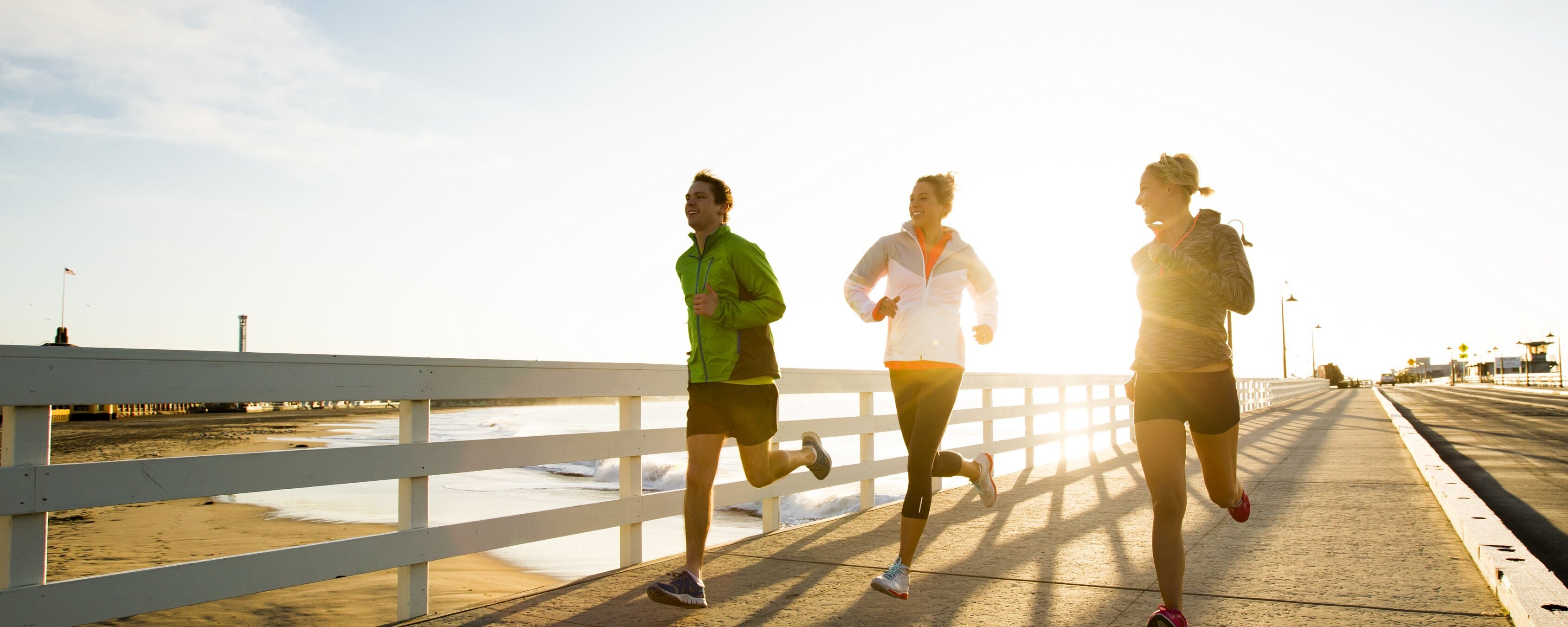Drei Personen laufen bei Sonnenschein an der Strandpromenade entlang. 
