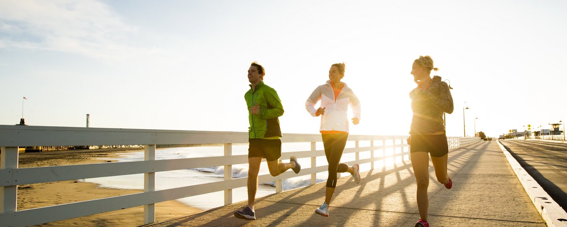 Drei Personen laufen bei Sonnenschein an der Strandpromenade entlang. 