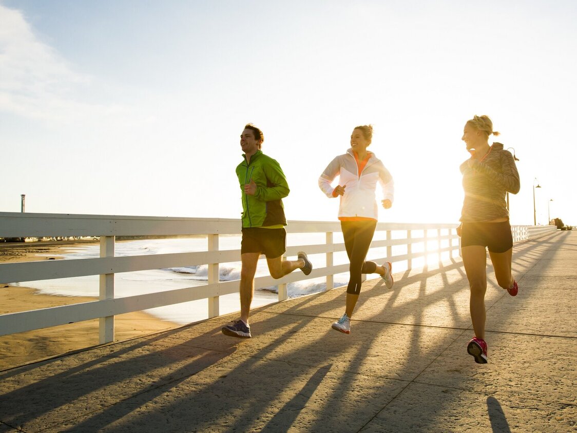 Drei Personen laufen bei Sonnenschein an der Strandpromenade entlang. 
