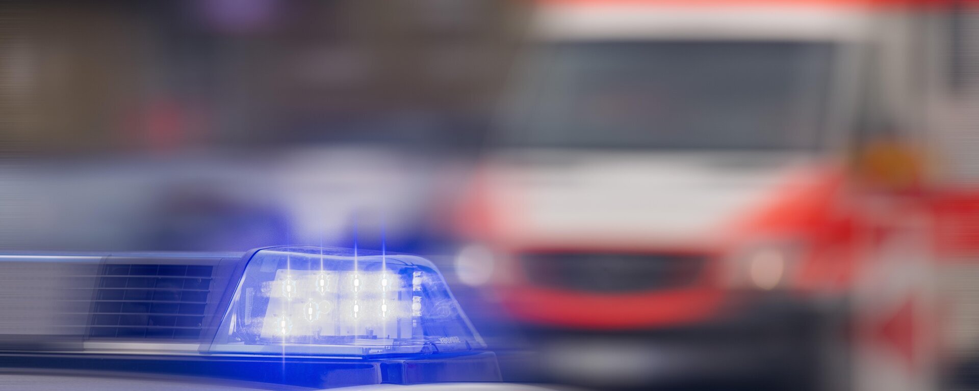 Ein verschwommenes Bild. Im Vordergrund sieht man Blaulicht und im Hintergrund einen Krankenwagen.