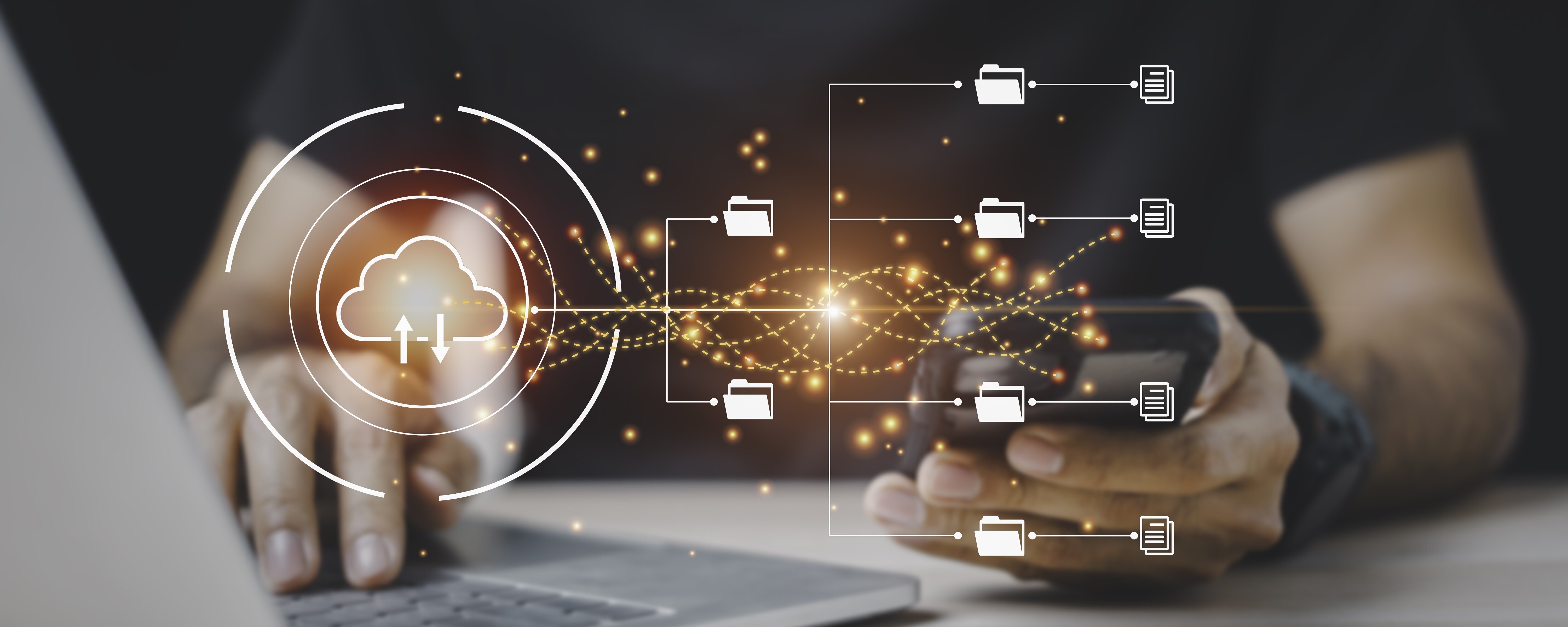 Jemand tippt auf einem Laptop und hat dabei ein Handy in der anderen Hand. Im Vordergrund werden virtuelle Symbole angezeigt.