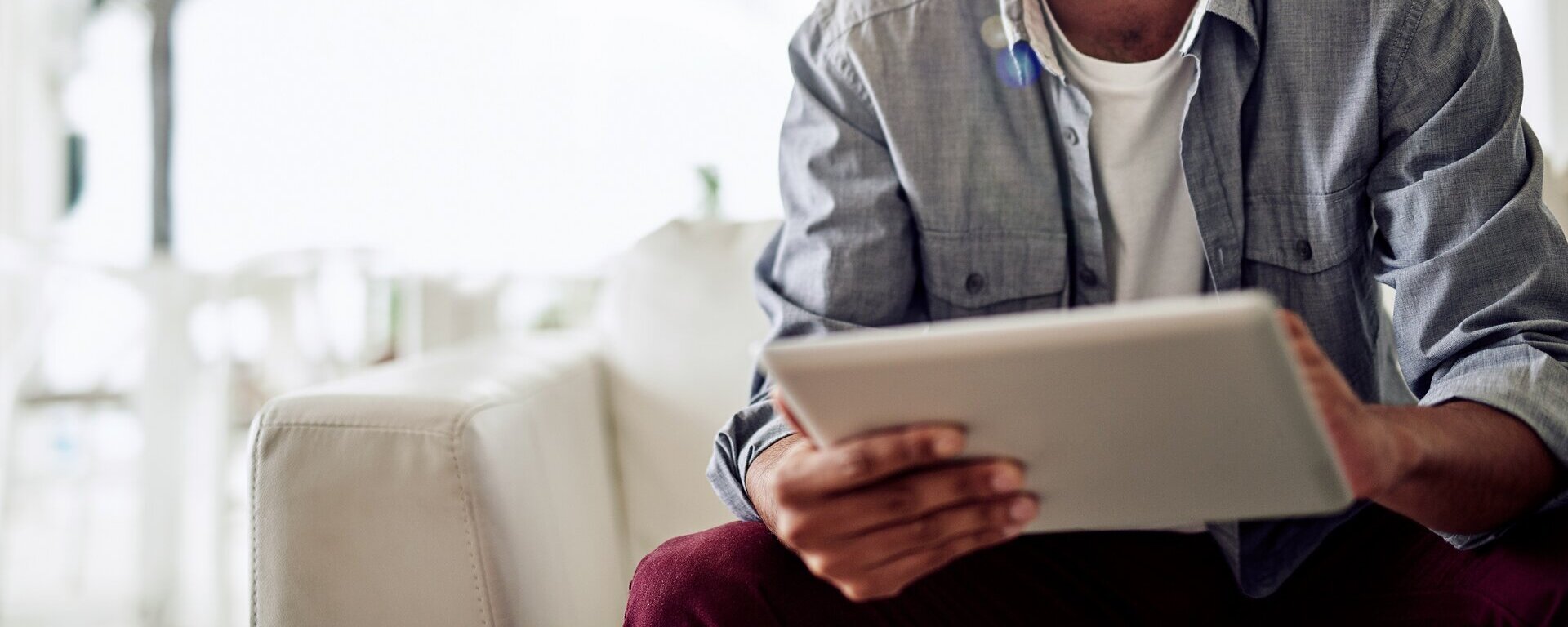 Ein Mann sitzt auf dem Sofa und schaut auf ein Tablet.