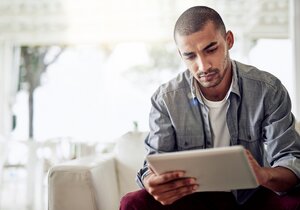 Ein Mann sitzt auf dem Sofa und schaut auf ein Tablet.