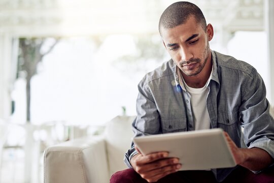 Ein Mann sitzt auf dem Sofa und schaut auf ein Tablet.