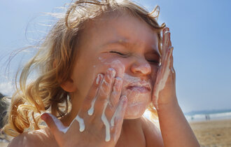 Ein Kind cremt sich mit Sonnenmilch im Gesicht ein.