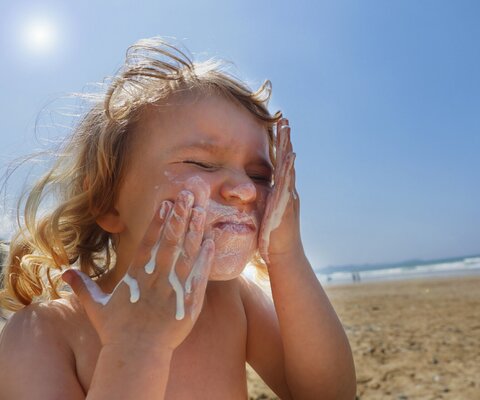 Ein Kind cremt sich mit Sonnenmilch im Gesicht ein.