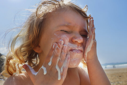 Ein Kind cremt sich mit Sonnenmilch im Gesicht ein.