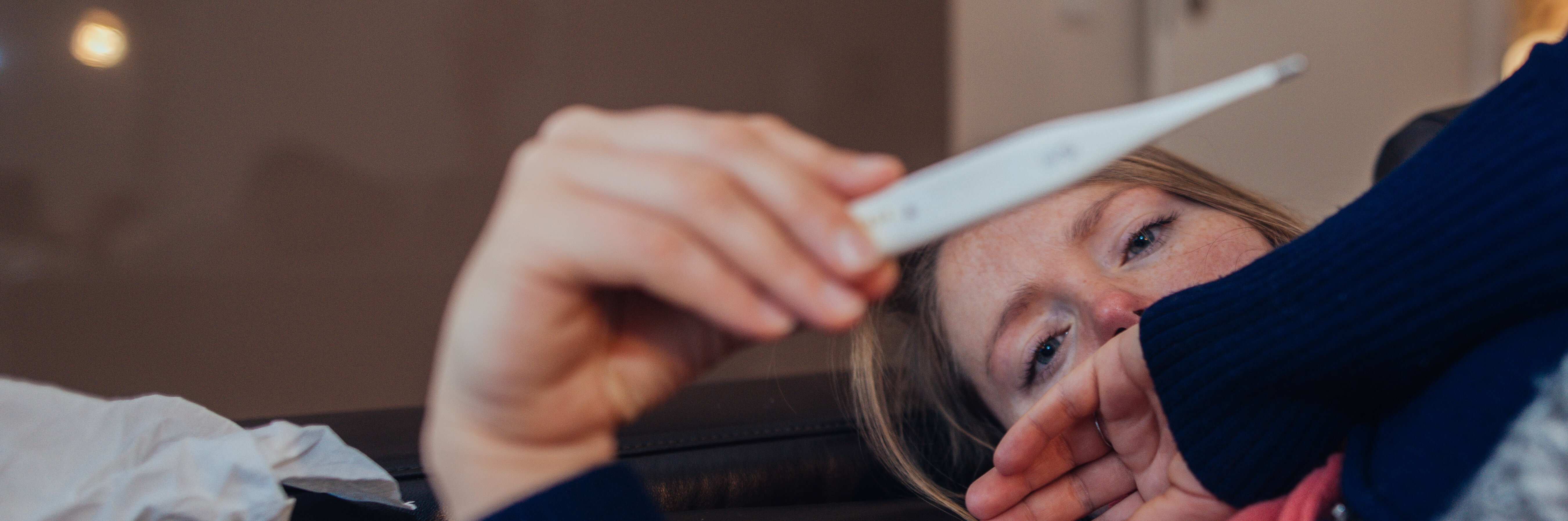 Kranke Frau, die zu Hause auf das Thermometer schaut.