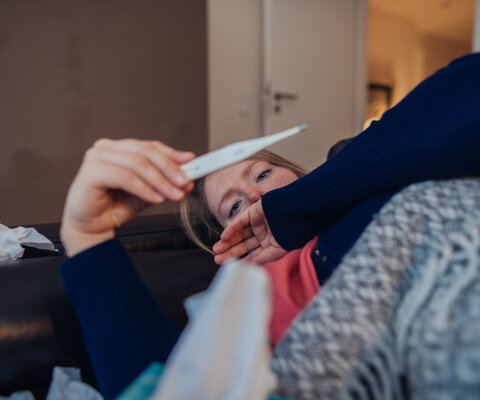 Kranke Frau, die zu Hause auf das Thermometer schaut.