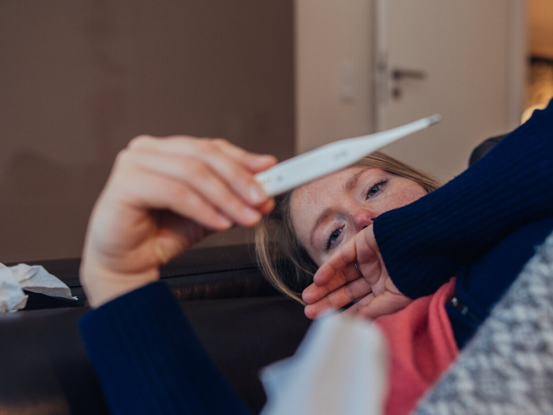 Kranke Frau, die zu Hause auf das Thermometer schaut.