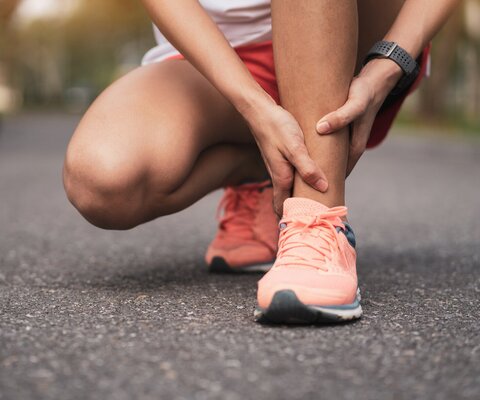 Eine Frau in Joggingkleidung kniet und hält sich das Fußgelenk.