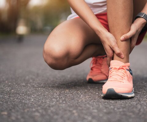 Eine Frau in Joggingkleidung kniet und hält sich das Fußgelenk.