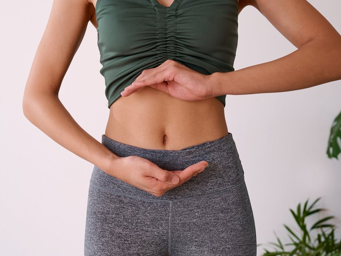 Sportliche Frau umrahmt ihren Bauch mit den Händen.