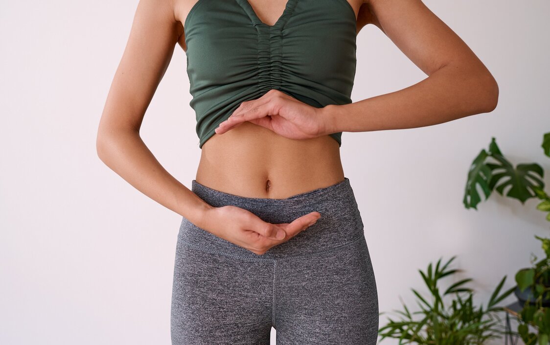 Sportliche Frau umrahmt ihren Bauch mit den Händen.
