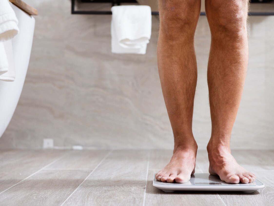 Ein Mann steht im Bad auf einer Waage. Man sieht lediglich die Beine.