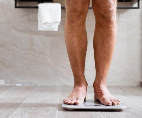 Ein Mann steht im Bad auf einer Waage. Man sieht lediglich die Beine.