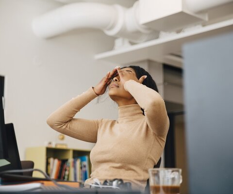 Eine Frau hält sich die Hände über den Kopf. Sie sitzt an ihrem Arbeitsplatz vor einem PC.