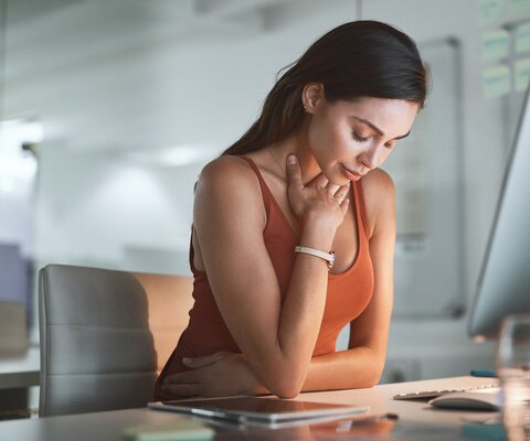 Eine Frau sitzt am Schreibtisch und hält ihre Hand an ihren Hals.