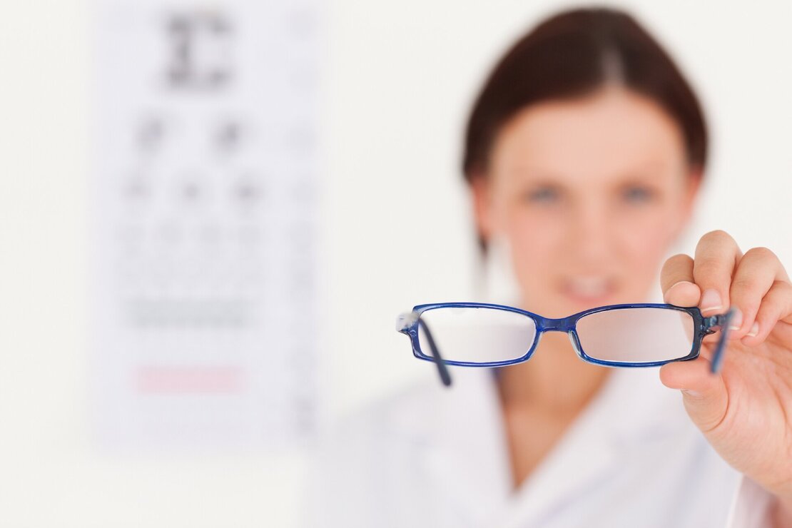 Nahaufnahme einer Brille, die von einer Optikerin in die Kamera gehalten wird
