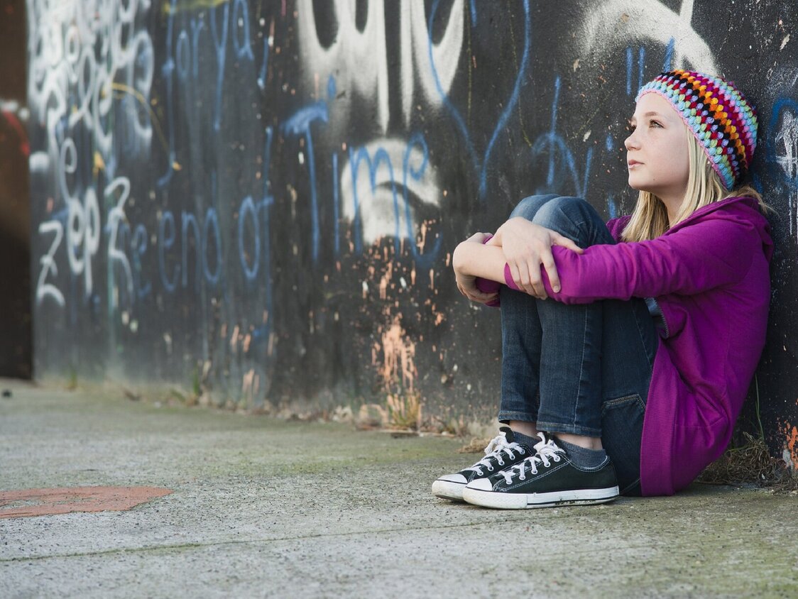 Ein jugendliches Mädchen sitzt nachdenklich vor einer Graffiti-Wand.