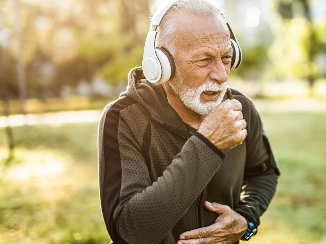 Ein älterer Mann hustet draußen beim Sport.