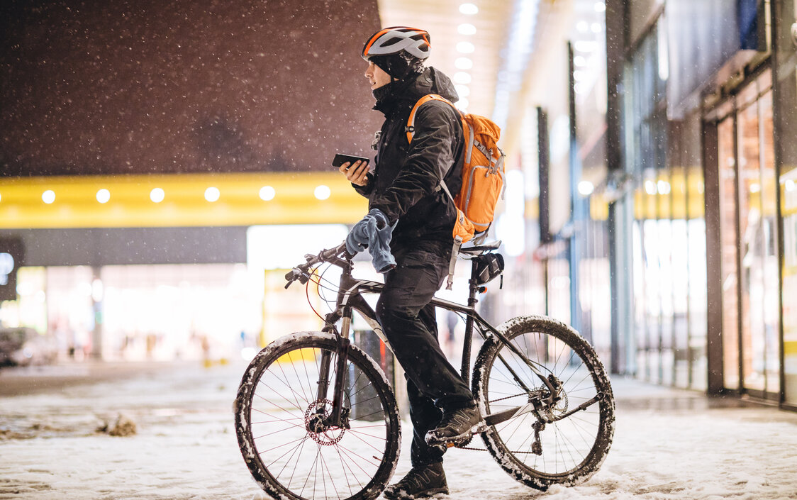 Ein Mann auf einem Fahrrad steht in einer verschneiten Stadt und hat sein Handy in der Hand.