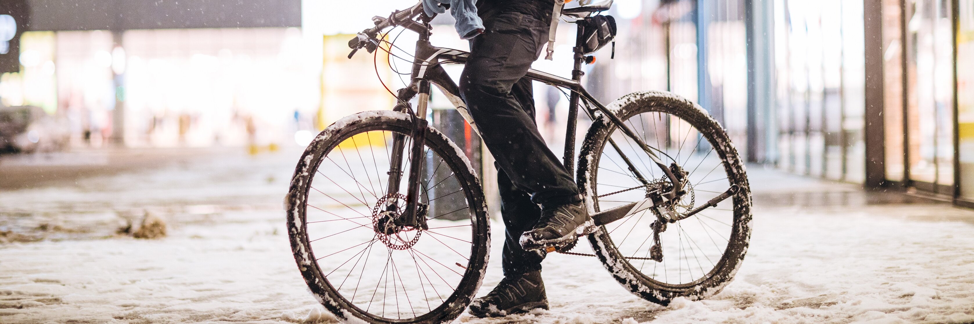 Ein Mann auf einem Fahrrad steht in einer verschneiten Stadt und hat sein Handy in der Hand.
