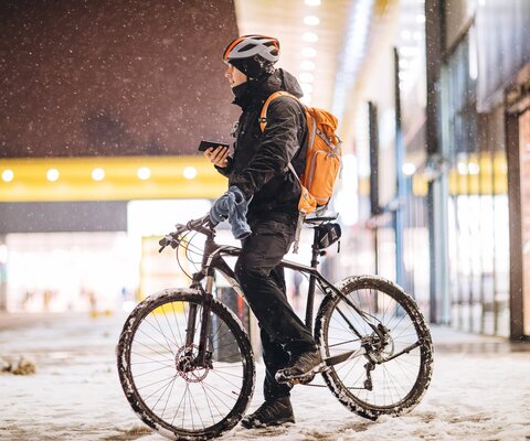 Ein Mann auf einem Fahrrad steht in einer verschneiten Stadt und hat sein Handy in der Hand.