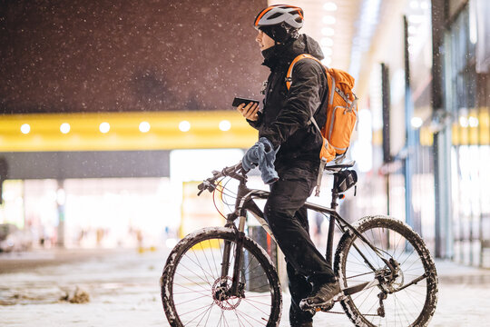 Ein Mann auf einem Fahrrad steht in einer verschneiten Stadt und hat sein Handy in der Hand.