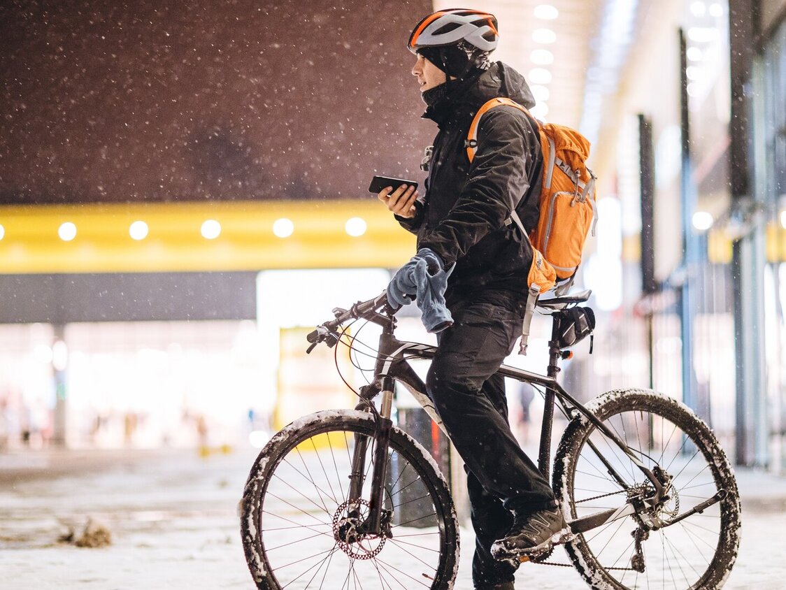 Ein Mann auf einem Fahrrad steht in einer verschneiten Stadt und hat sein Handy in der Hand.