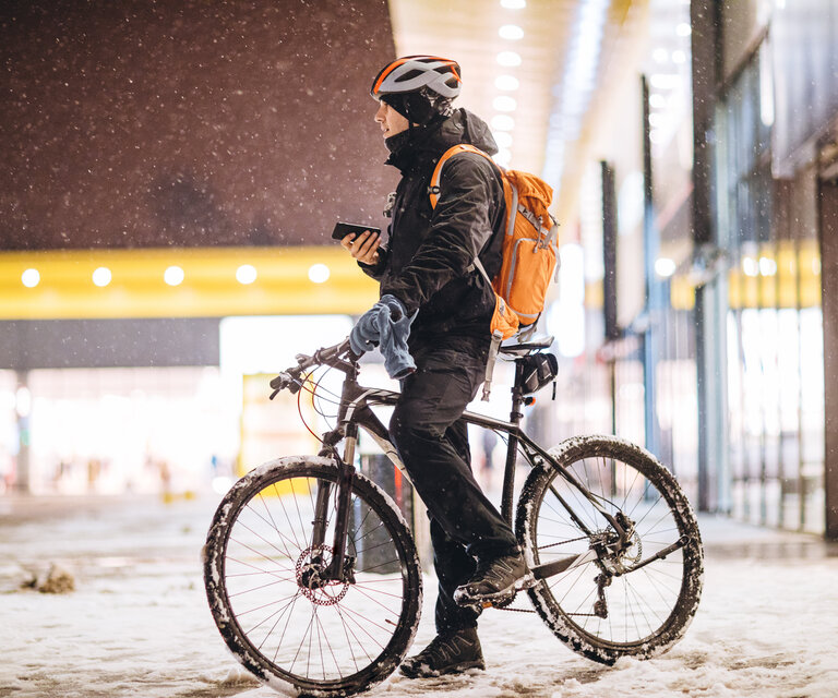 Ein Mann auf einem Fahrrad steht in einer verschneiten Stadt und hat sein Handy in der Hand.