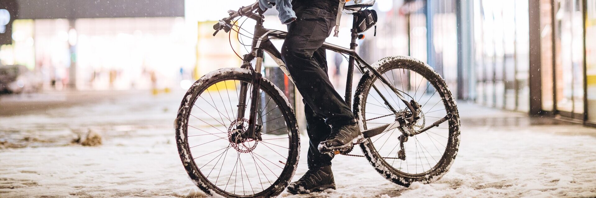 Ein Mann auf einem Fahrrad steht in einer verschneiten Stadt und hat sein Handy in der Hand.
